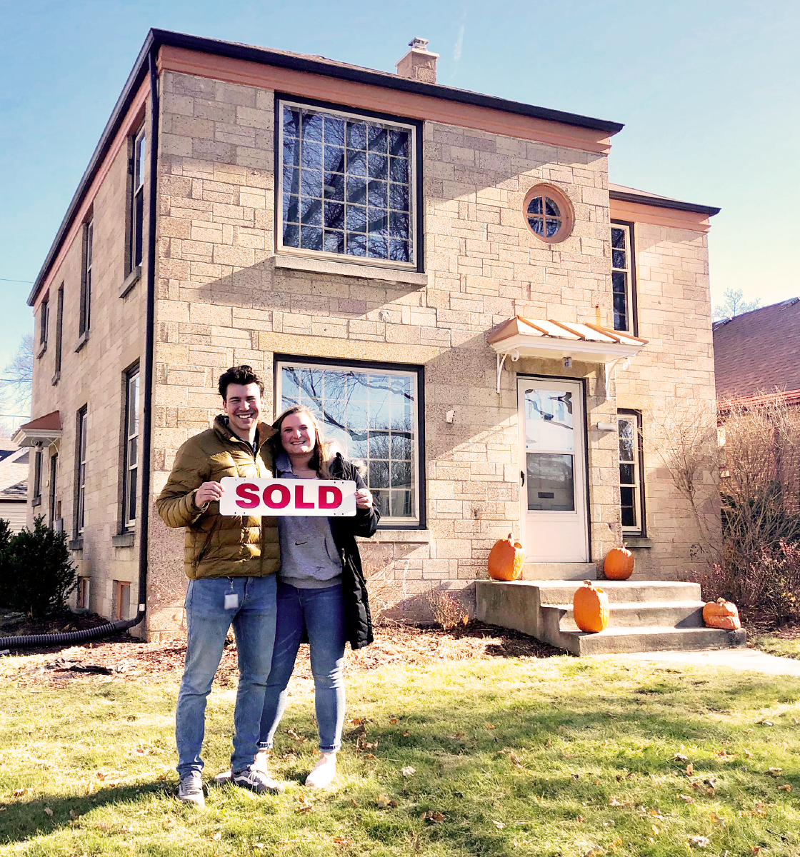 Smiling couple with sold sign in front of new house