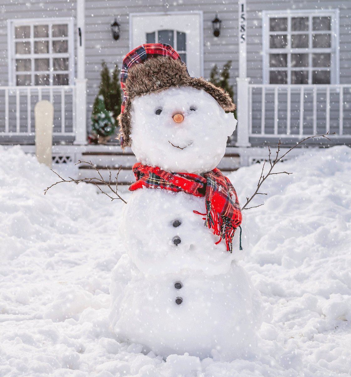 Happy snowman with red scarf in front of a home in winter