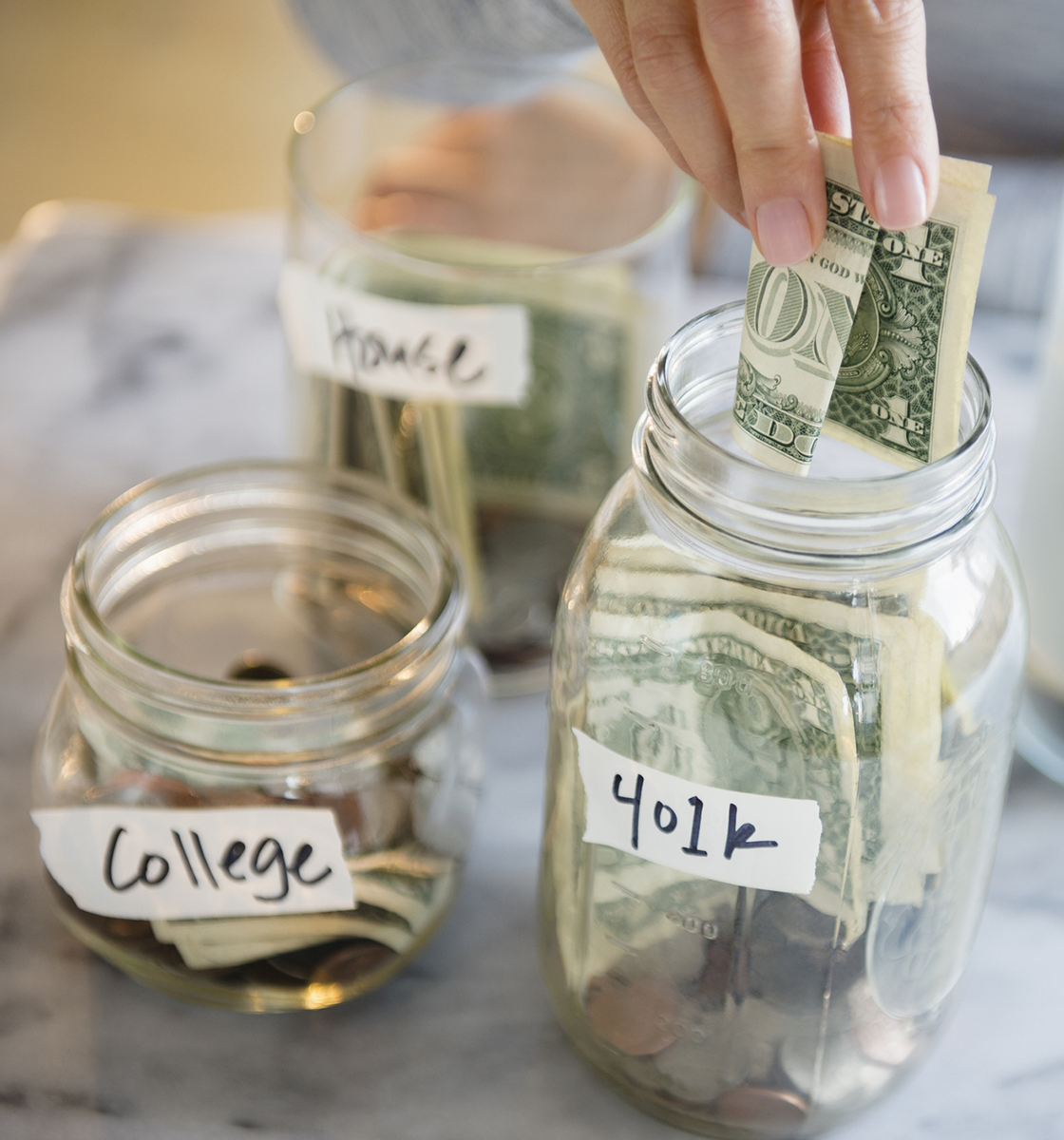 woman pulls money from a jar labeled retirement; other jars with money are labeled house and college